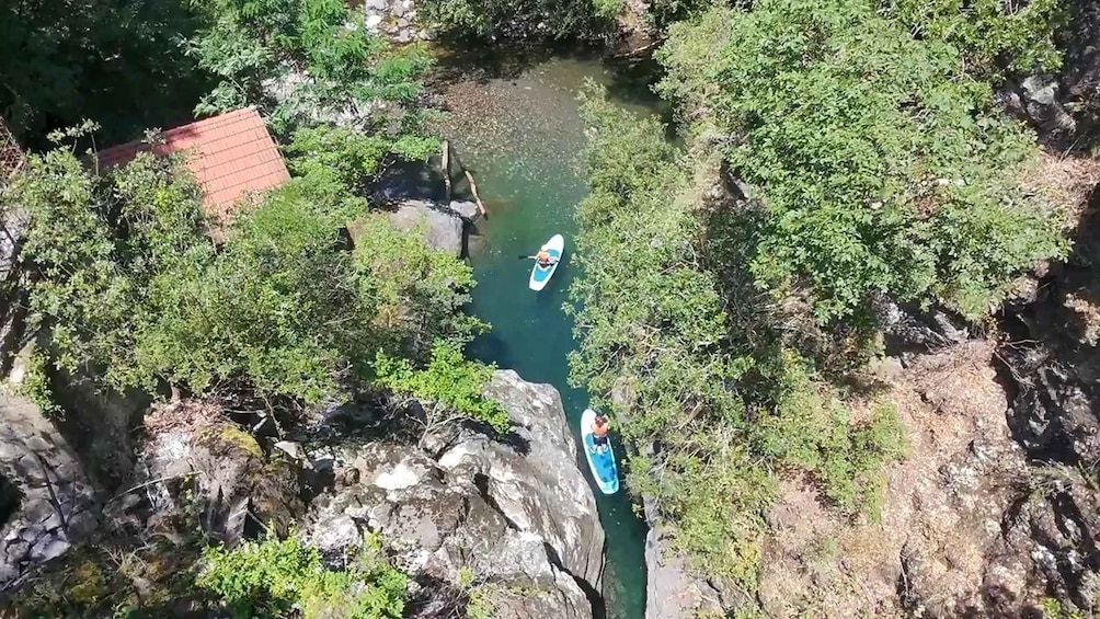Two kayaks on a narrow river surrounded by dense foliage and rocky terrain. 1