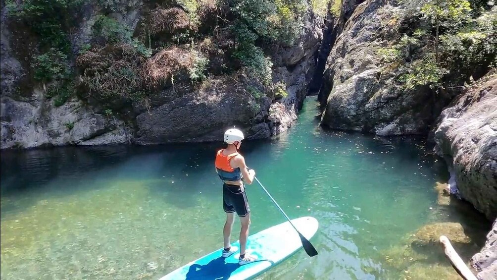 A person standing on a paddleboard in a river surrounded by rocky cliffs. 3