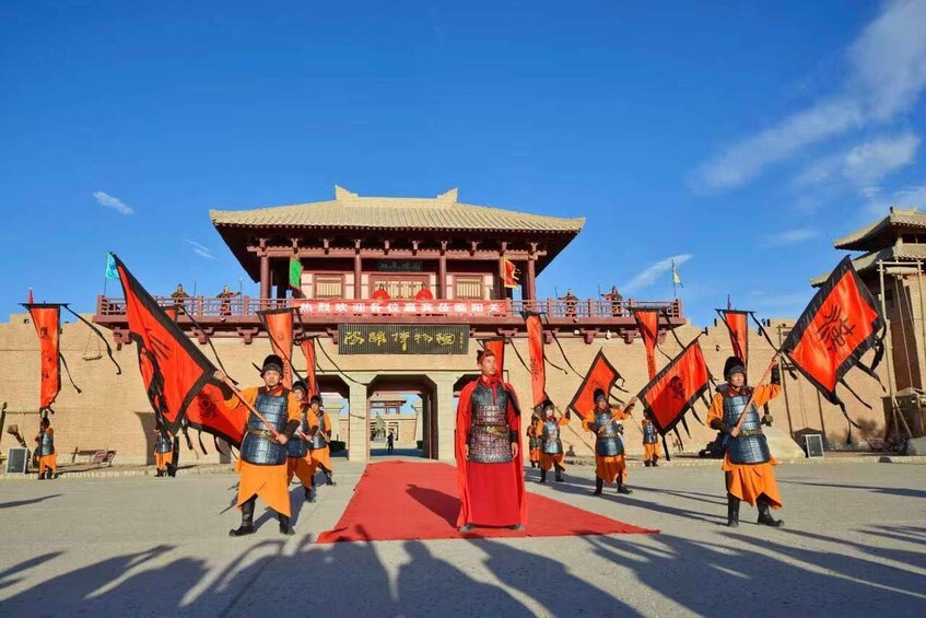 A group of performers in traditional costumes with flags in front of a historical building. 1