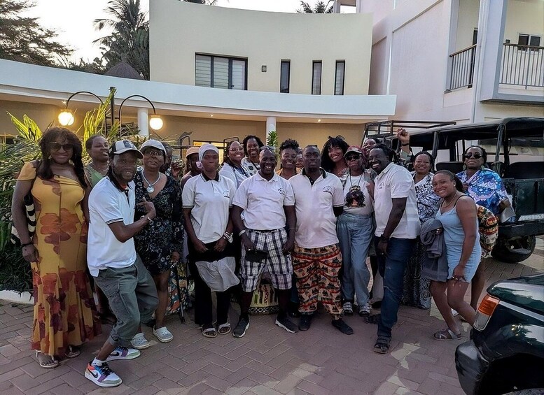 A group of people posing in front of a building with a balcony and a parked vehicle. 5