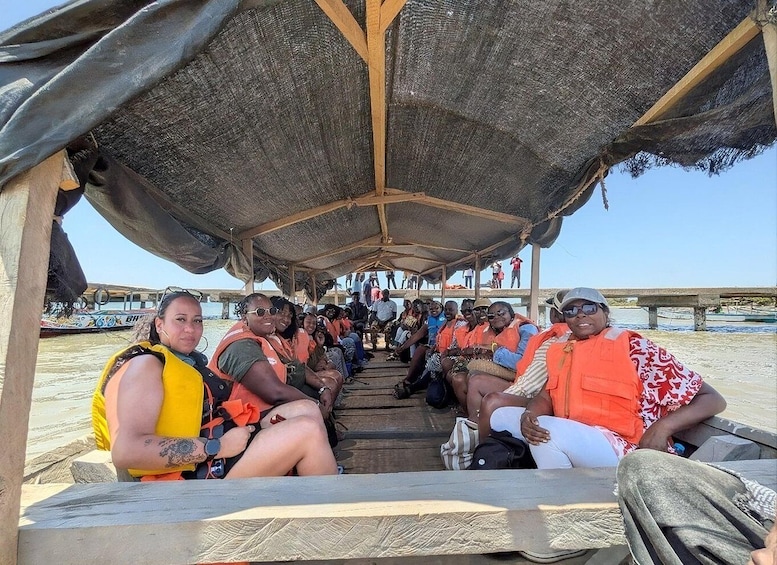 A group of people seated under a thatched roof structure on a beach. 4