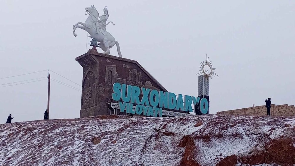A statue of a man on a horse, a sign reading 'Surxondaryo,' and a sun-shaped structure. 4