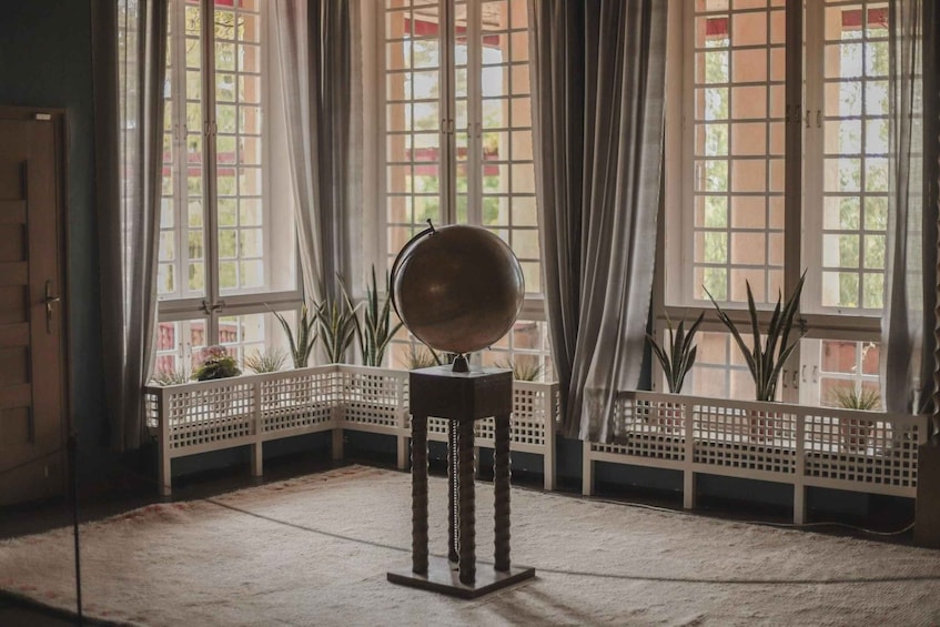 A globe on a stand in a room with large windows and plants. 5