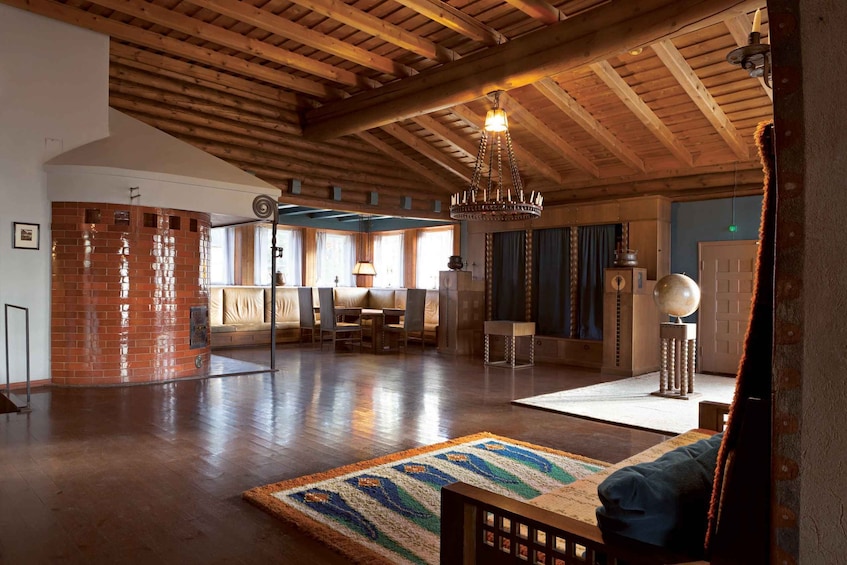 A spacious room with wooden beams, a brick wall, a chandelier, and a patterned rug. 3
