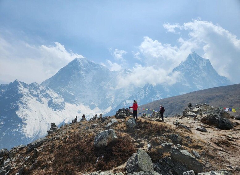 A mountainous landscape with trekkers on a rocky path, snow-capped peaks in the background, and a clear sky. 3