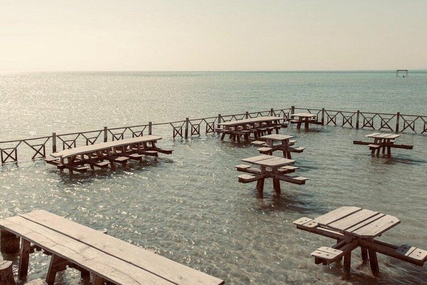 Ein Strand mit Holztischen zum Picknick und einem hölzernen Steg, der ins Wasser ragt. 4