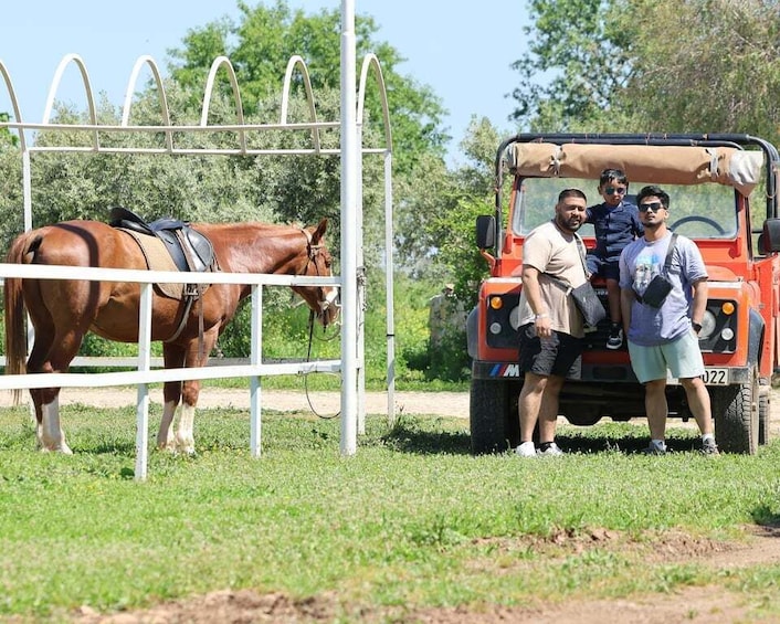 A horse in a fenced area, a red vehicle, and three people standing beside it. 2