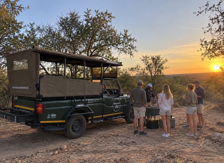A safari vehicle with a covered top, parked on a dirt road with people standing nearby. 3