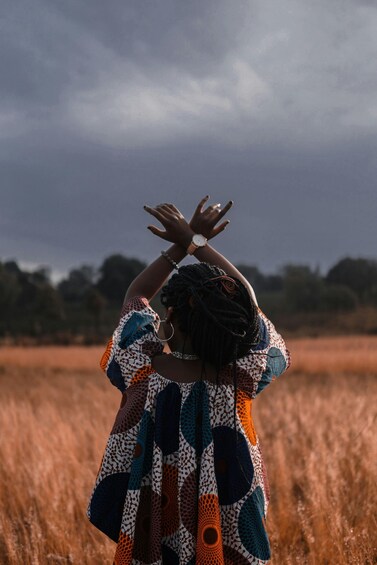 A person in a colorful dress standing in a field with a cloudy sky. 2