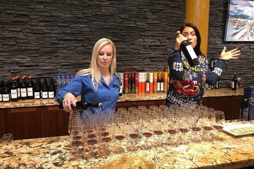 A bartender pouring wine into glasses on a counter with bottles and a stone wall in the background. 1