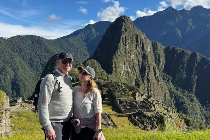 Dos personas frente a las ruinas de Machu Picchu, con montañas al fondo. 1