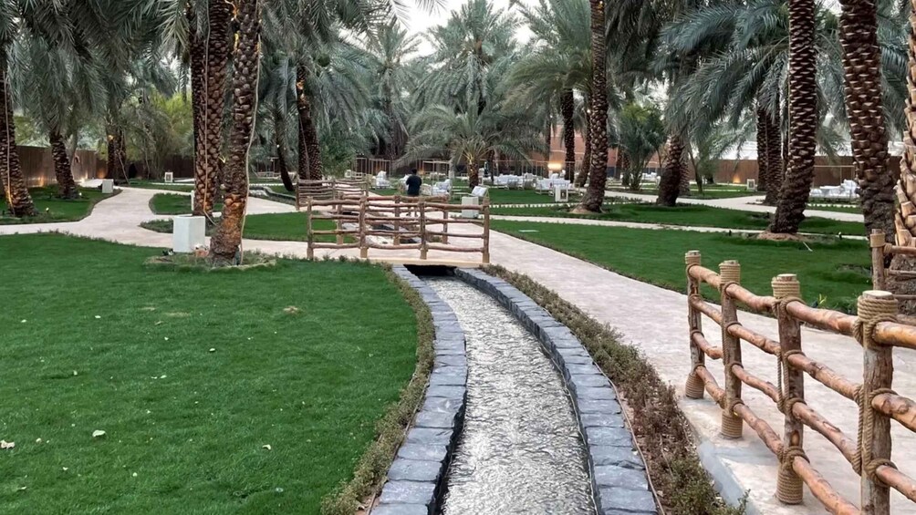 A pathway flanked by palm trees and a wooden fence, leading to a distant area with structures. 5