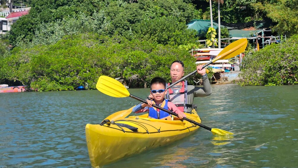 A person in a yellow kayak on a river, surrounded by greenery and buildings. 4