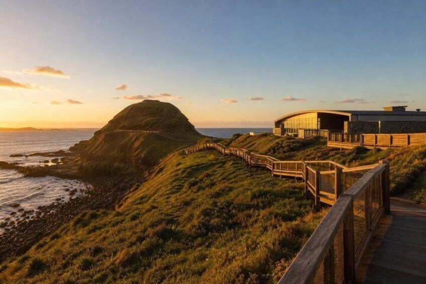 A coastal landscape with a grassy hill, a wooden walkway, and a modern building with a curved roof. 4