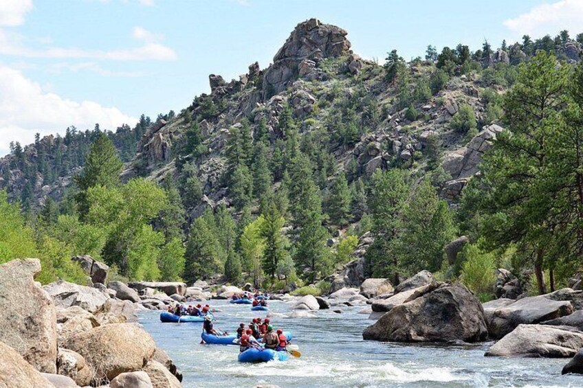 A river with people rafting, surrounded by rocky terrain and trees. 1
