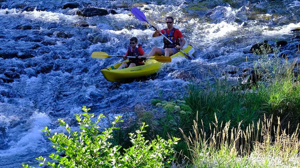 Two people kayaking on a river with rapids. 1