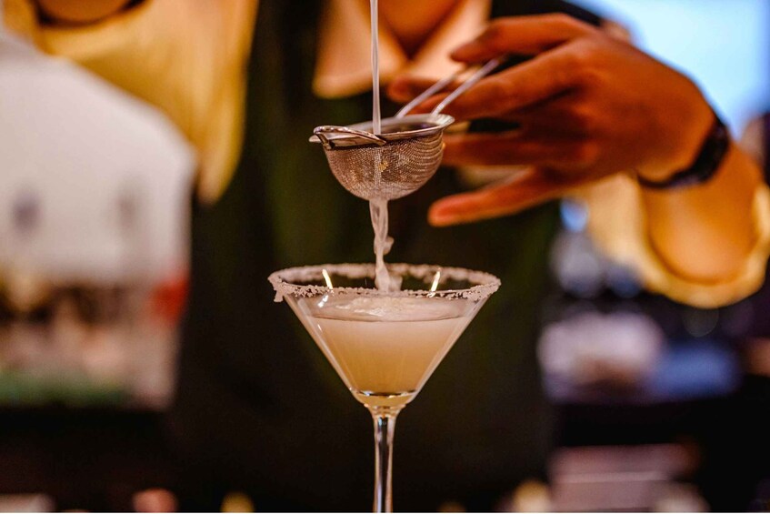 A bartender pouring a drink into a martini glass. 1