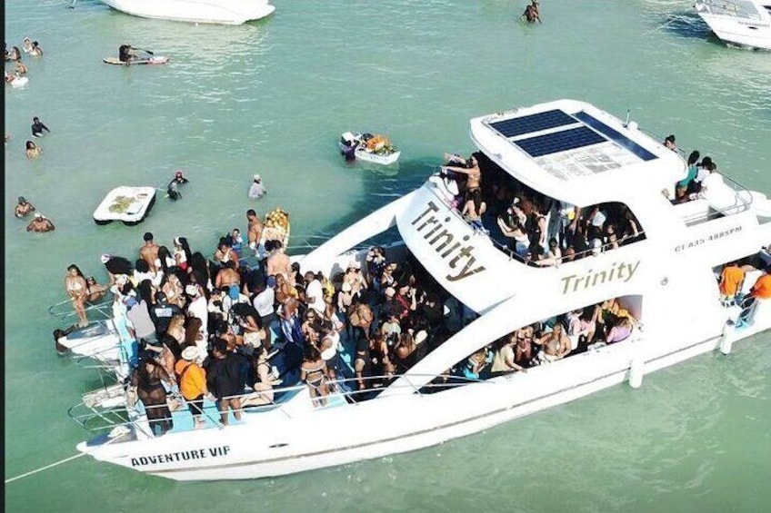 Una embarcación abarrotada llamada 'Trinity' con la inscripción 'Adventure VIP' en el costado, rodeada de otras embarcaciones en el agua. 1