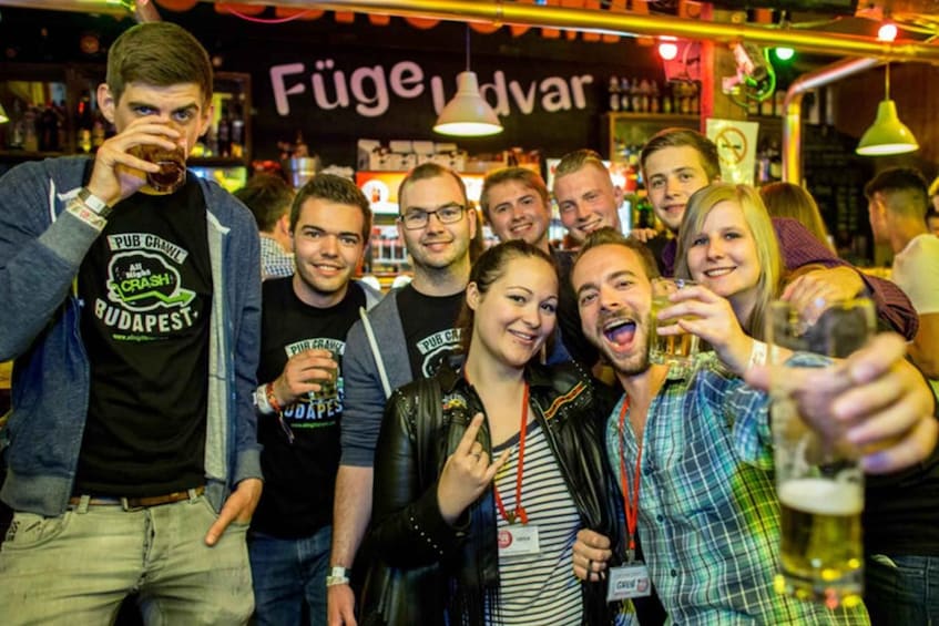 A group of people in a bar with a sign that reads 'Füge Udvar'. 2