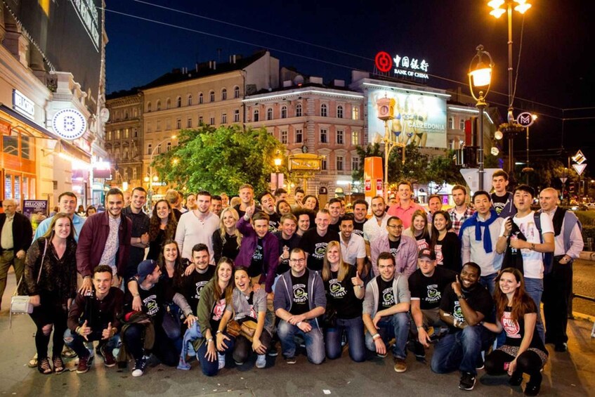 A group of people posing for a photo in an urban setting with historic buildings and street lamps. 3