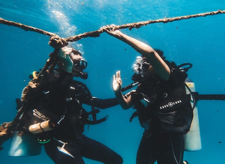 Two scuba divers underwater, connected by a rope, with one making a hand gesture. 1