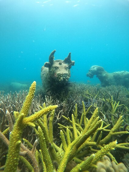 An underwater scene with a large bull statue and a smaller statue in the background, surrounded by coral. 2