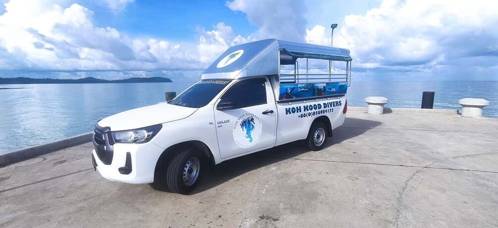A white truck with a blue logo and text 'KOH KOO DIVERS' parked by a waterfront. 4