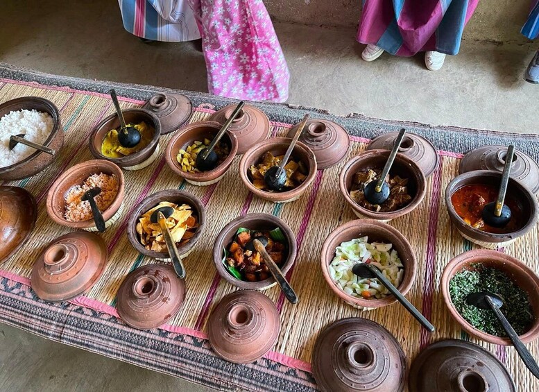 A variety of traditional clay pots with food and utensils on a woven mat. 3