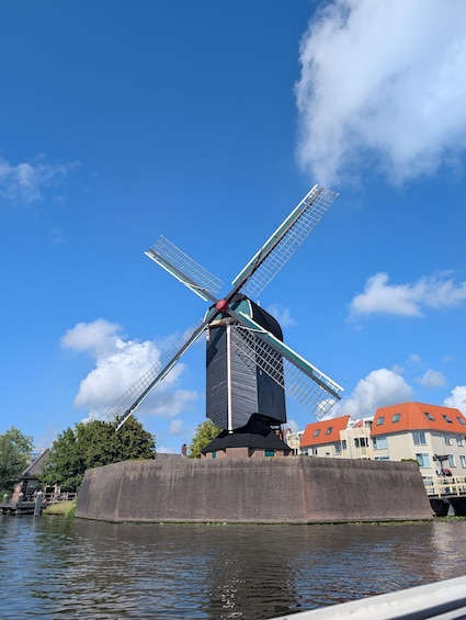 A windmill with a red top, situated by a canal with buildings in the background. 2