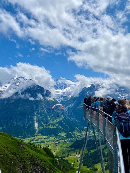 A group of people observing a paraglider flying over a mountainous landscape with snow-capped peaks and a clear blue sky. 2
