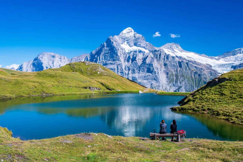 A lake with mountains in the background and two people sitting on a bench. 1