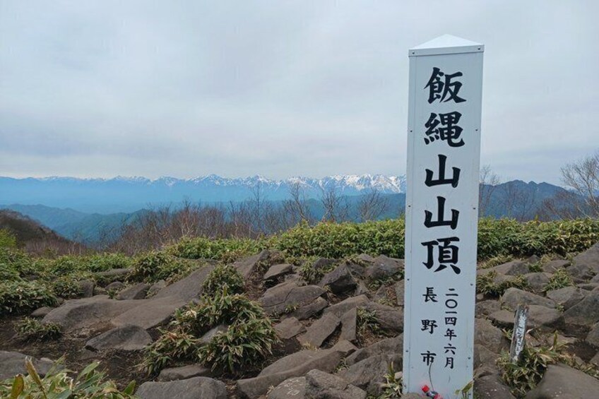 A signpost with Japanese characters, set against a mountainous backdrop with snow-capped peaks. 2