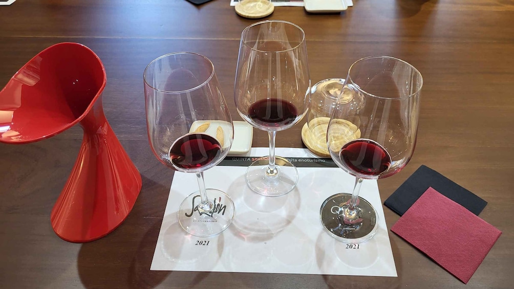Three wine glasses with red wine on a table, a red funnel, and a menu. 5