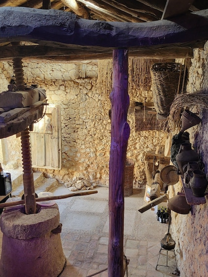 A rustic stone building with a wooden door, a stone mill, and various traditional pottery and tools. 3