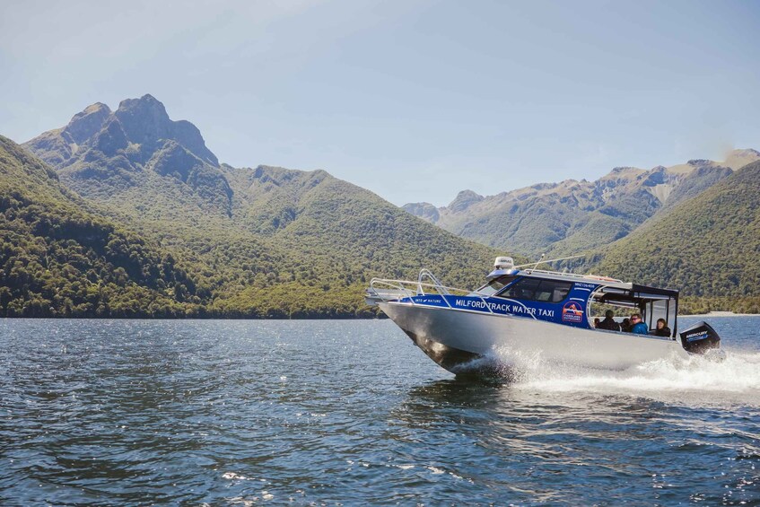 A boat named 'Milford Track Water Taxi' on a lake with mountains in the background. 4