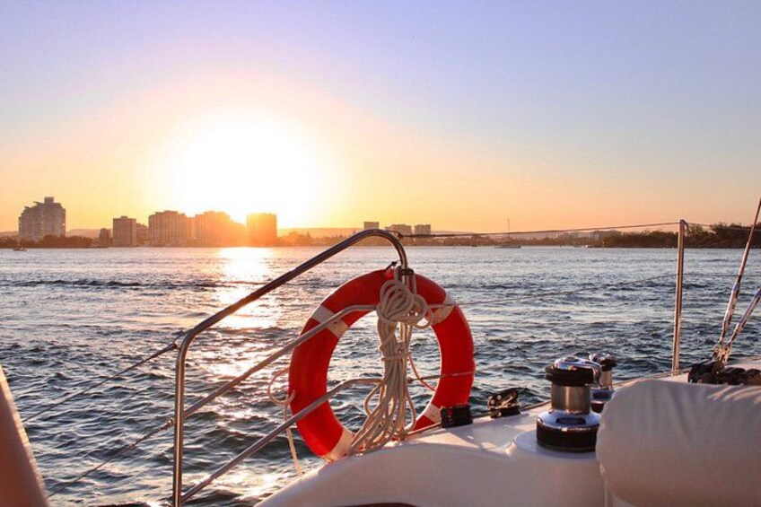 A boat with a lifebuoy and ropes, water, and a city skyline in the background. 2