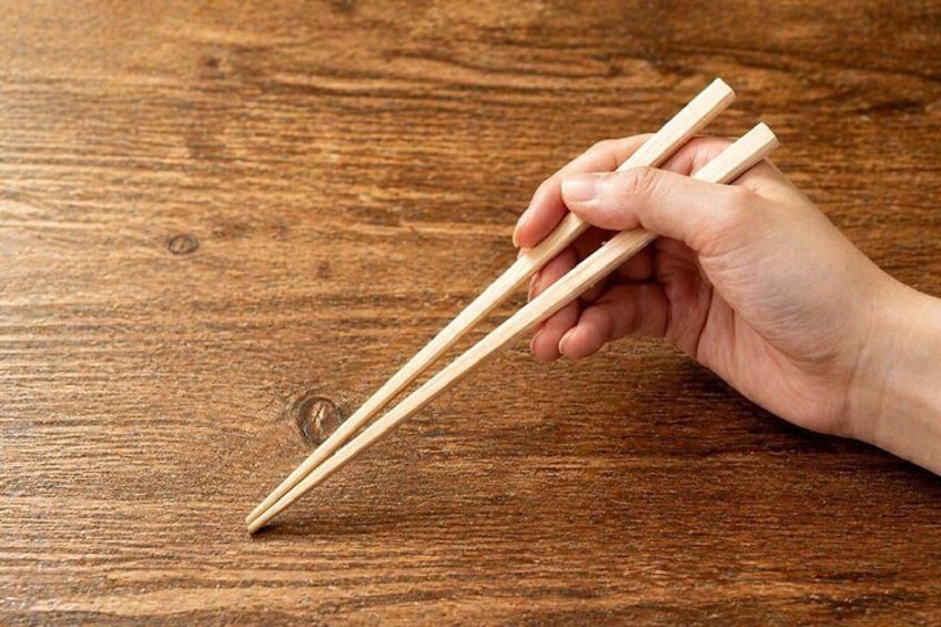 Una mano sosteniendo palillos sobre una mesa de madera. 2