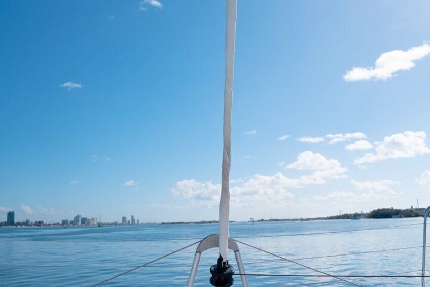 Un voilier à la voile blanche sur une eau calme, sous un ciel dégagé, avec une silhouette de ville visible au loin. 2