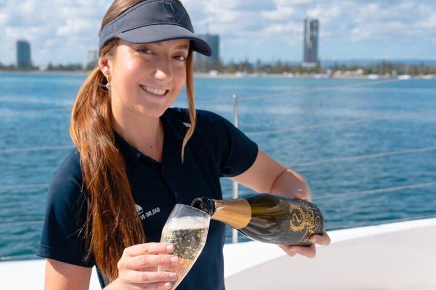 Une personne verse du champagne dans un verre à bord d’un bateau, avec la silhouette d’une ville en arrière-plan. 5