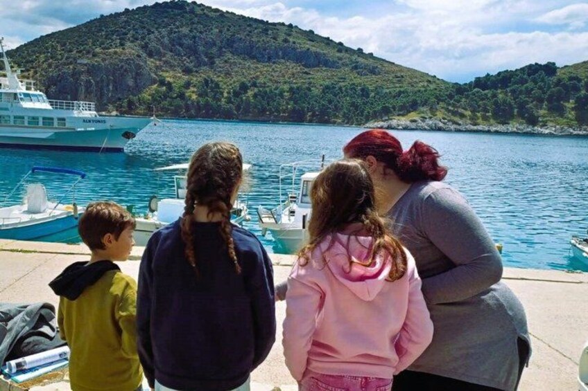 A group of people by a body of water with a boat and a hilly landscape in the background. 3