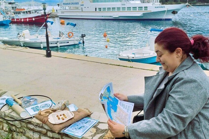 A person reading a brochure by a waterfront with boats and a large ship in the background. 2
