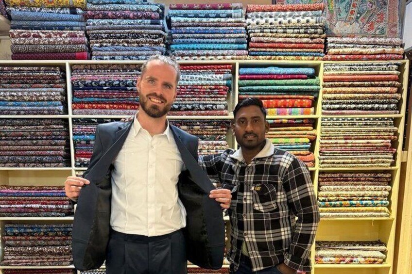 Två män i en textilbutik, omgivna av hyllor fulla med färgglada tyger. 1
