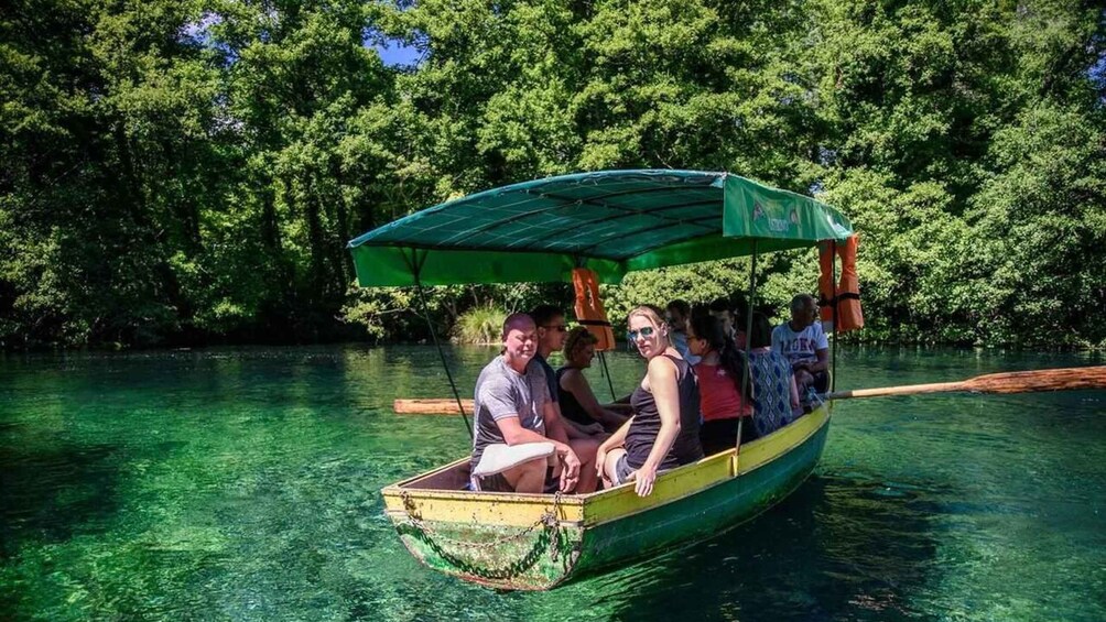 A group of people in a boat with a canopy, surrounded by dense green foliage and clear water. 3