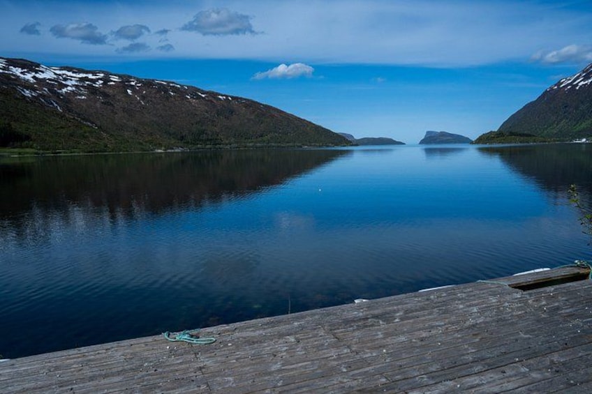 Un lago calmo con un molo di legno, circondato da montagne con chiazze di neve. 2