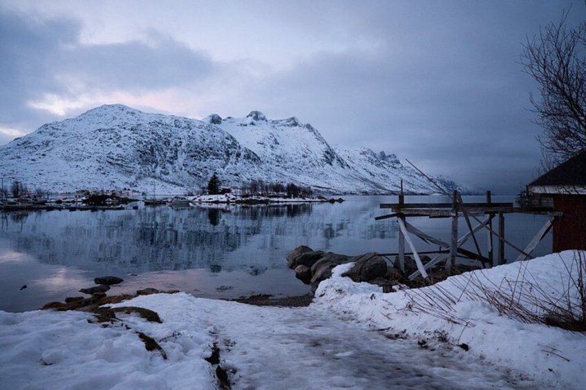 Paesaggio innevato con un lago tranquillo, un pontile di legno e una montagna sullo sfondo. 1