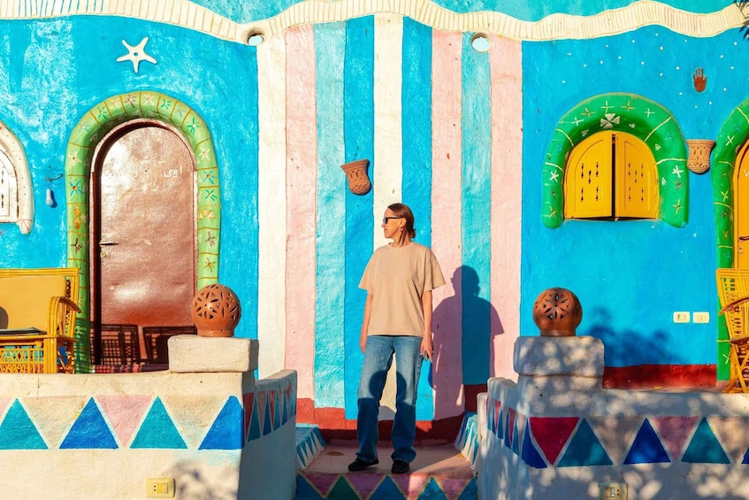 A person standing in front of a colorful building with striped walls, a large arched door, and decorative pottery. 4