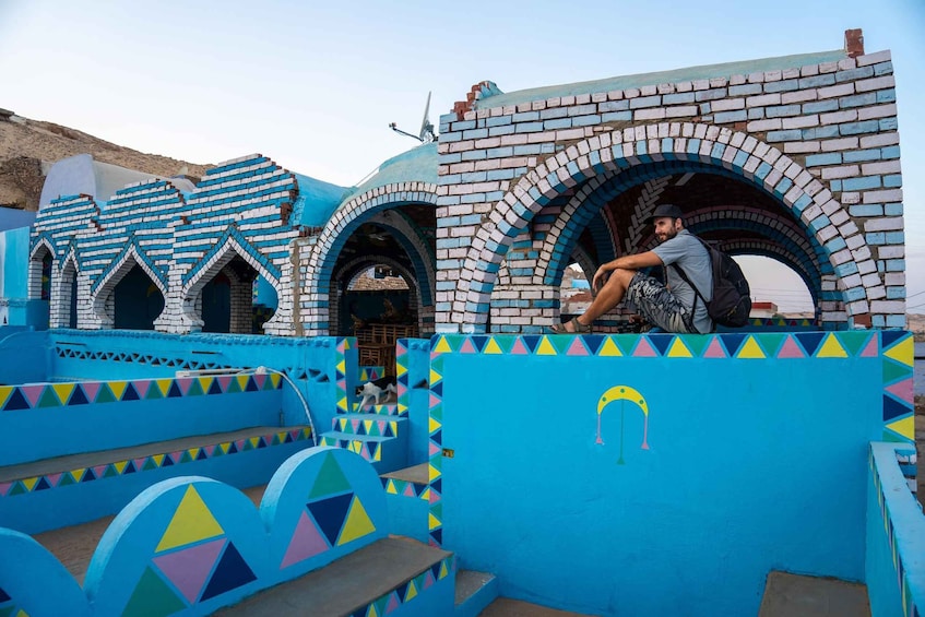 A colorful building with blue and white brick arches and walls, and a person sitting on a ledge. 1