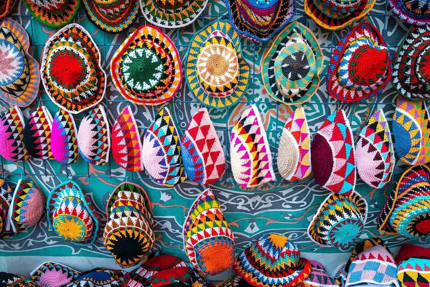 A variety of colorful crocheted hats and headwear displayed on a patterned wall. 5