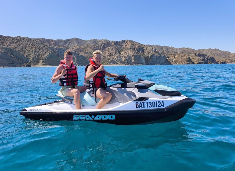 Two people on a Sea-Doo jet ski with a mountainous landscape in the background. 1