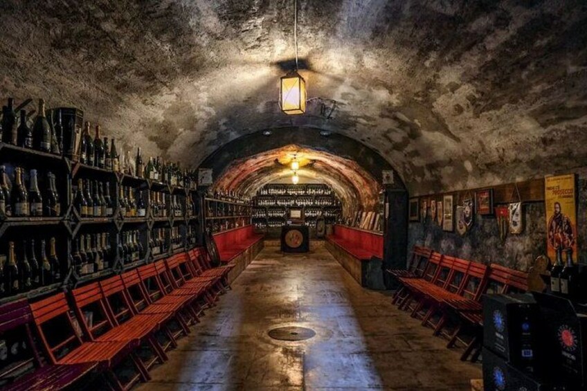 An underground bar with wooden benches and shelves of bottles. 2